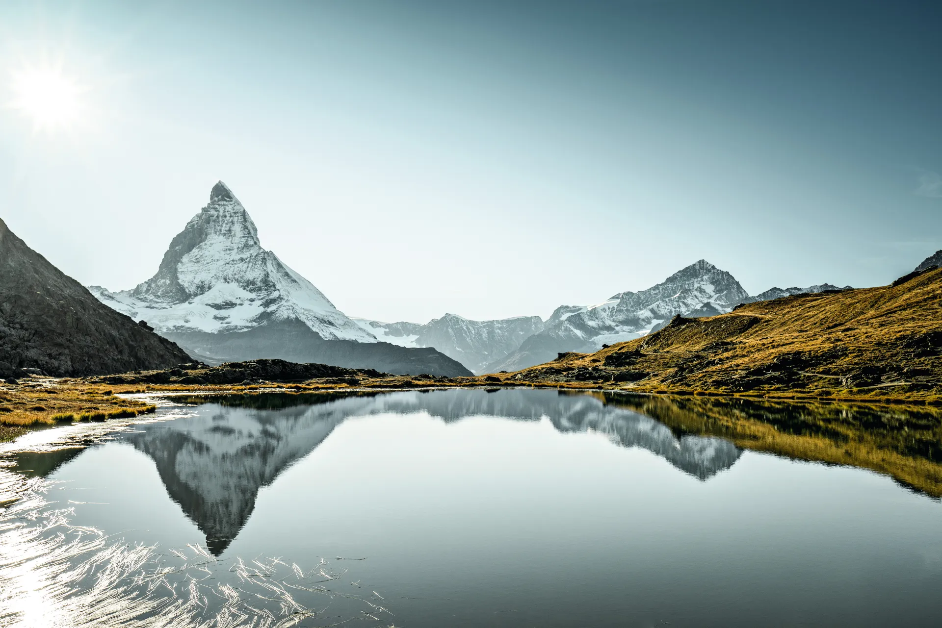 Le Cervin se reflète dans un lac de montagne, avec un ciel bleu en arrière-plan.
