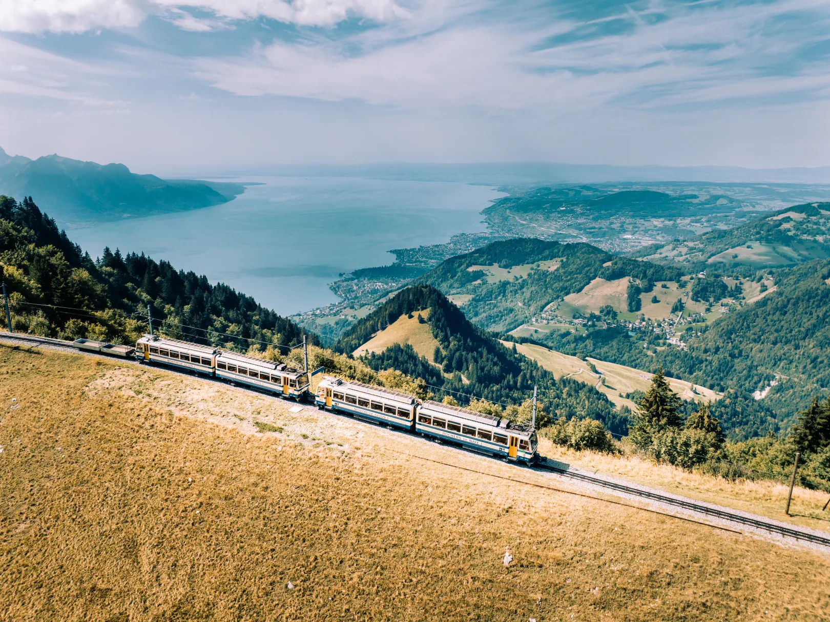 Le téléphérique Rochers-de-Naye traverse des collines verdoyantes au-dessus du lac Léman, avec une large vue sur le lac et le paysage environnant.