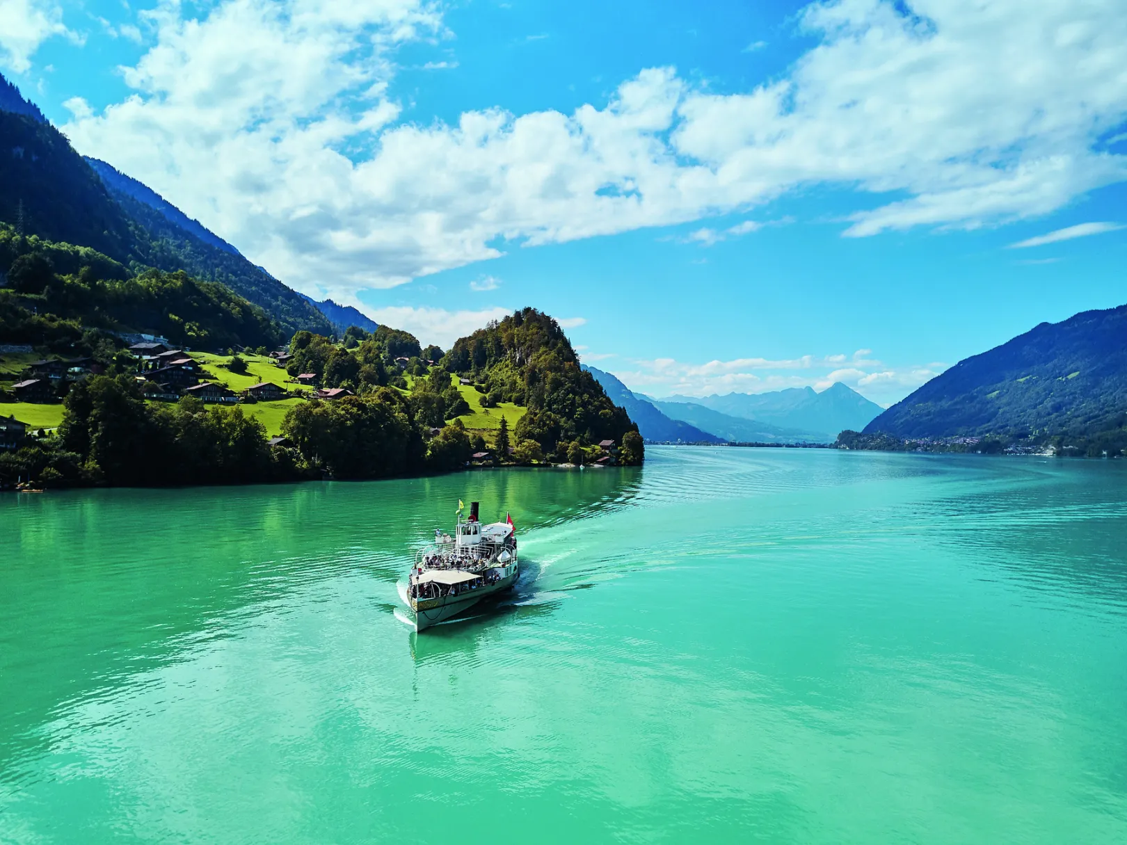 Le bateau à vapeur de BLS Schifffahrt navigue en été sur le lac de Brienz, avec en arrière-plan un décor montagneux alpin.